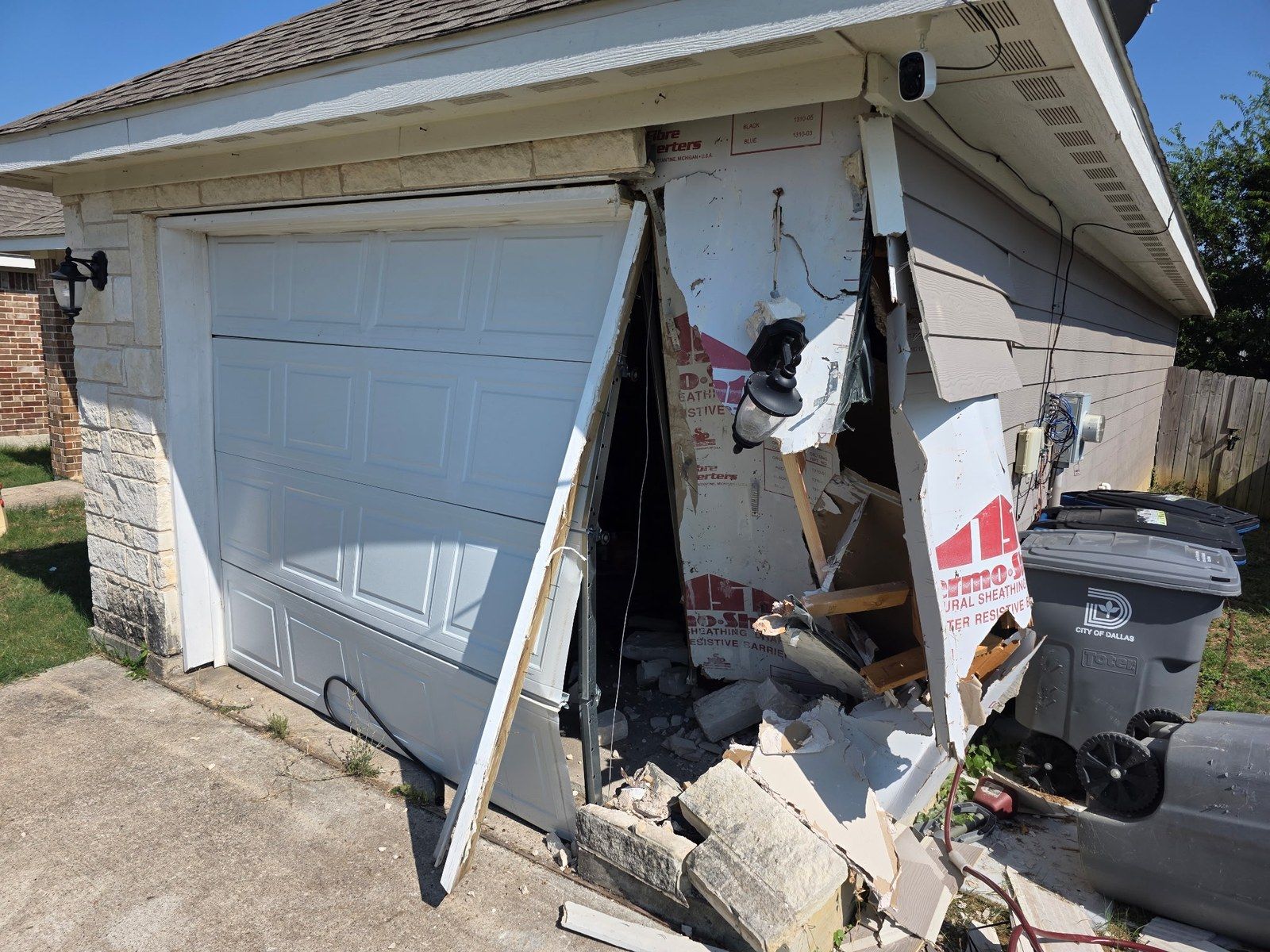 Detached garage with the wall caved in and the door knocked loose after a vehicle impact