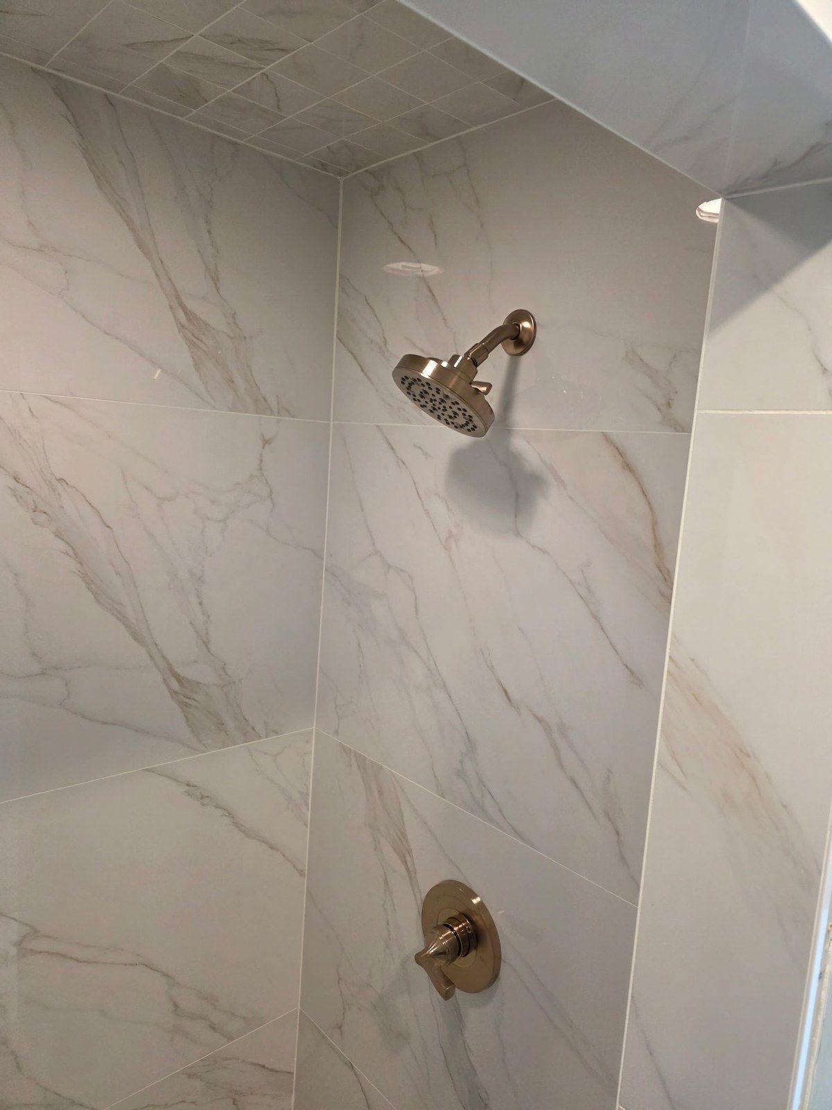 Marble-look tile shower with brushed-gold shower head and valve