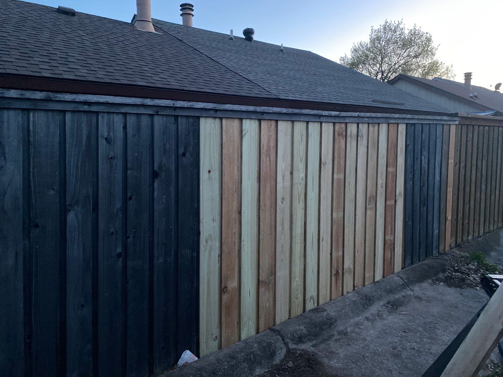 Wood privacy fence after repair, with new pickets stained dark