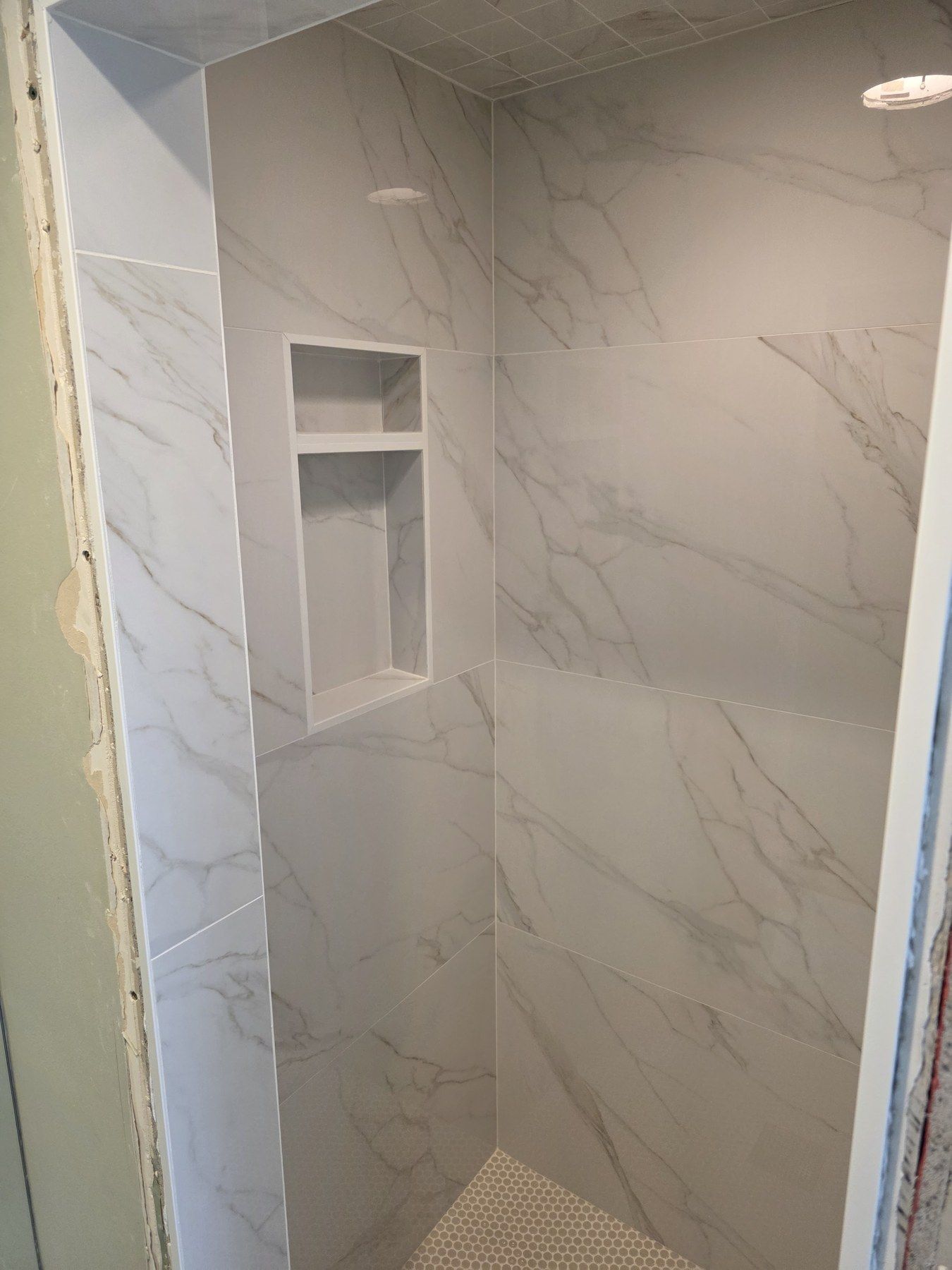 Finished shower with large marble-look wall tile and a recessed niche