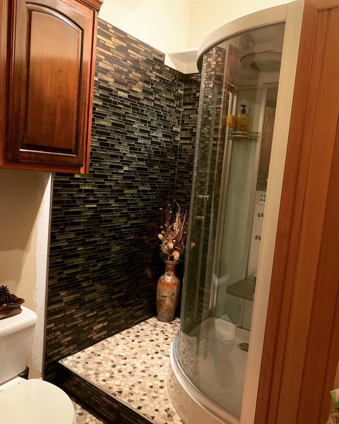 Bathroom with a dark glass mosaic wall, round shower and wood cabinets