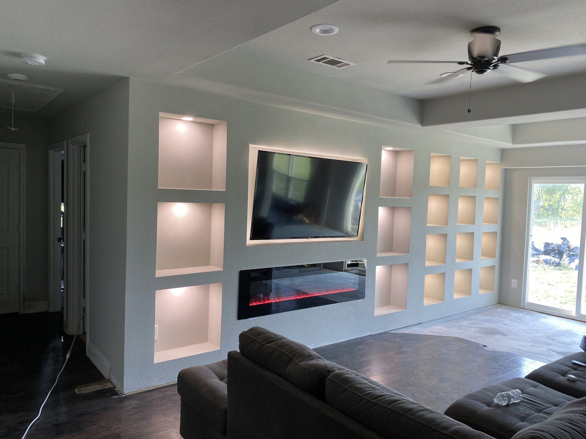 Finished living room media wall with lit niches, wall-mounted TV and a linear fireplace