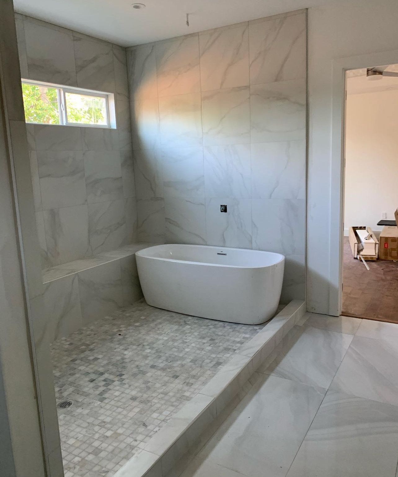 Walk-in wet room with a freestanding tub, large marble-look tile and mosaic floor
